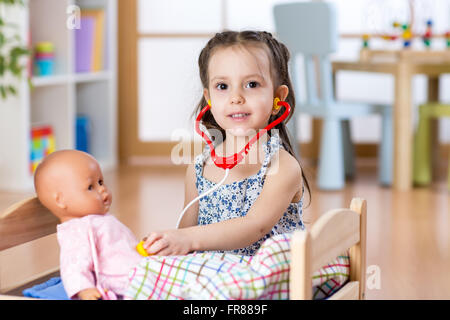 Kid toddler playing rôle médecin examinant sa poupée à l'aide de jeu de stéthoscope de jeux à la maison, à l'école ou au jardin d'enfants Banque D'Images