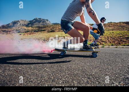 L'homme et la femme longboard en bas de la route. Vue latérale des jeunes pratiquer le patinage à l'extérieur sur la route. Banque D'Images