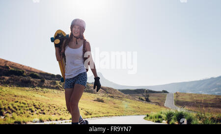 Happy young woman walking avec un longboard sur route de campagne. Patineur professionnel à l'extérieur sur une journée ensoleillée.