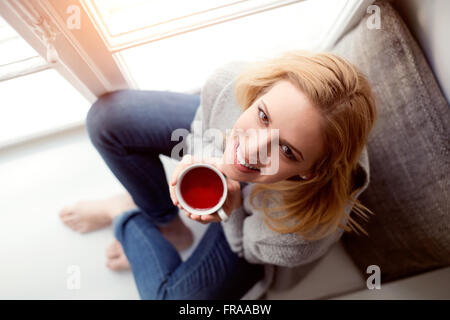 Femme sur appui de fenêtre tenant une tasse de thé Banque D'Images