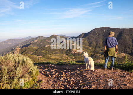 Lumière dorée illumine randonneur et chien sur le sentier de crête de grès à Circle X Ranch au coucher du soleil Banque D'Images