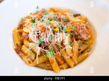 Une assiette de penne pollo (poulet) les pâtes en sauce tomate et poivron rouge avec le Parmigiano Reggiano, le bacon de sanglier, et des germes. Banque D'Images