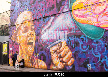 Trois adolescentes debout devant un mur avec une grande zone d'écriture graffiti représentant un garçon crier avec un haut-parleur. Banque D'Images