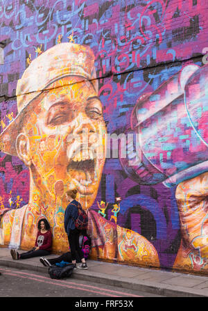 Trois adolescentes debout devant un mur avec une grande zone d'écriture graffiti représentant un garçon crier avec un haut-parleur. Banque D'Images