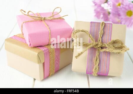 Cadeaux faits main de groupe avec papier marron et rose wrap sur table en bois blanc avec des fleurs Banque D'Images