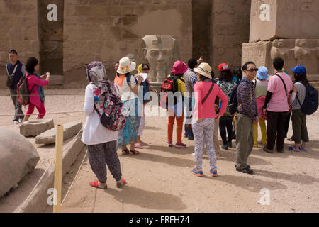 Les groupes de touristes se lever et photographie sous les colosses géant dans la cour de Ramsès II, à l'Egypte antique du temple de Louxor, vallée du Nil, en Égypte. Le temple a été construit par Amenhotep III, complété par Toutânkhamon puis ajouté à par Ramsès II. Vers l'arrière est un granit sanctuaire dédié à Alexandre le Grand et dans une autre partie, était un camp romain. Le temple a été presque continue à utiliser comme lieu de culte jusqu'à nos jours. Banque D'Images