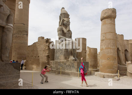 Les groupes de touristes se lever et photographie sous le colosse géant dans la cour de Ramsès II, à l'Egypte antique du temple de Louxor, vallée du Nil, en Égypte. Le temple a été construit par Amenhotep III, complété par Toutânkhamon puis ajouté à par Ramsès II. Vers l'arrière est un granit sanctuaire dédié à Alexandre le Grand et dans une autre partie, était un camp romain. Le temple a été presque continue à utiliser comme lieu de culte jusqu'à nos jours. Banque D'Images