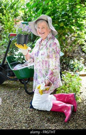 Cheerful senior woman holding potted plant in garden Banque D'Images