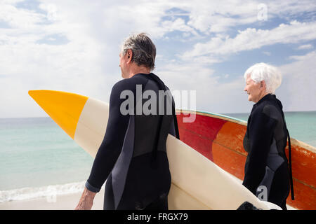 Senior couple in wetsuit holding surfboard on beach Banque D'Images