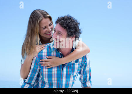 Man carrying woman on retour contre ciel bleu clair Banque D'Images