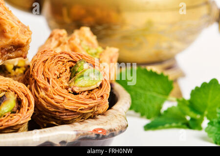 Libre d'un assortiment de différents baklava pâtisseries dans un bol en terre cuite sur une table et un verre d'or dans l'arrière-plan Banque D'Images