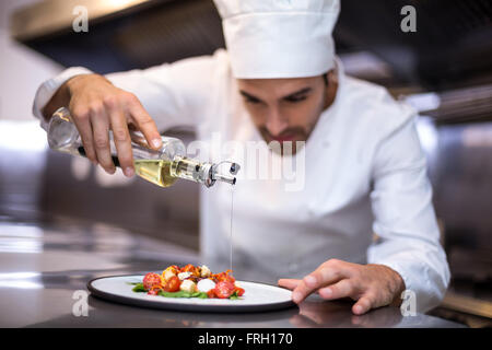Beau chef pouring olive oil sur les repas Banque D'Images
