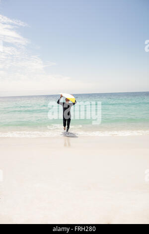 Man wetsuit running with surfboard sur sa tête Banque D'Images