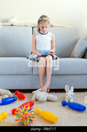 Il est temps de nettoyer vos jouets ! Little girl Playing with tablet pc, ne veulent pas faire le nettoyage. Banque D'Images