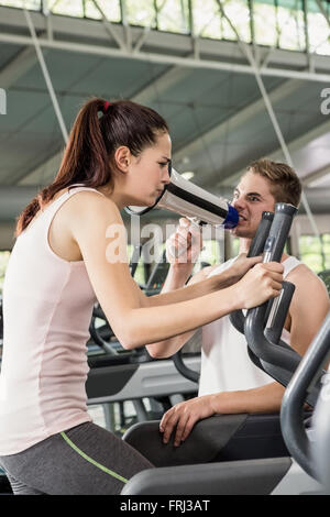 Avec un porte-voix crier formateur tout en femme exerçant sur une machine elliptique Banque D'Images