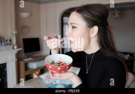 Jeune femme d'une vingtaine de manger sain bol de porridge au petit-déjeuner Banque D'Images