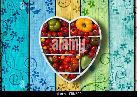 Divers les tomates en boîte en forme de coeur sur fond de bois peint en couleurs Banque D'Images