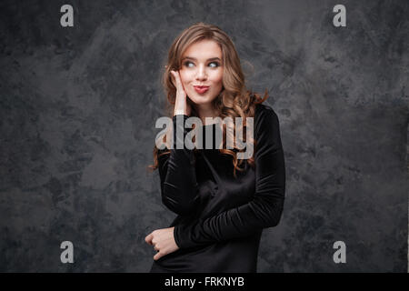 Jolie jeune femme amusante avec de longs cheveux bouclés making funny face de canard sur fond gris Banque D'Images