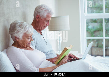 Senior woman reading book while man using laptop Banque D'Images