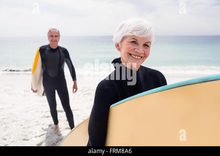 Senior couple in wetsuit holding surfboard on beach Banque D'Images