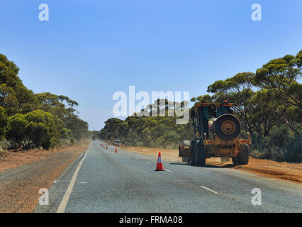 Les travaux routiers sur une route à l'ouest de l'Australie. Le tracteur de la machinerie lourde sur une route de gravier pavage côté derrière la limitation panneaux Banque D'Images