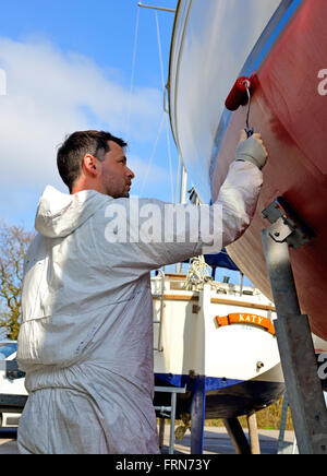 Marina yard travailleur peinture antifouling peinture (protection contre les mauvaises herbes marines) par rouleau sur un yacht à keeled pour la nouvelle saison de voile, Chichester, Royaume-Uni Banque D'Images