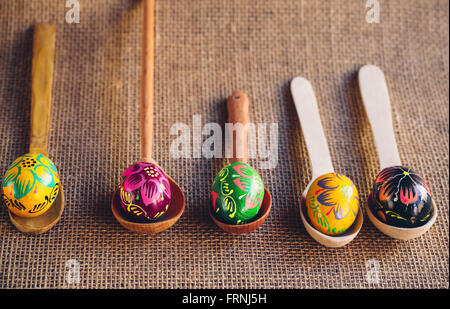 Les oeufs de Pâques colorés peints magnifiques couchés sur des cuillères en bois sur un fond de toile de jute Banque D'Images