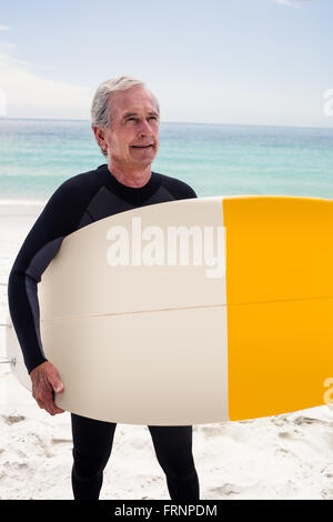 Happy senior man in wetsuit holding a surfboard Banque D'Images