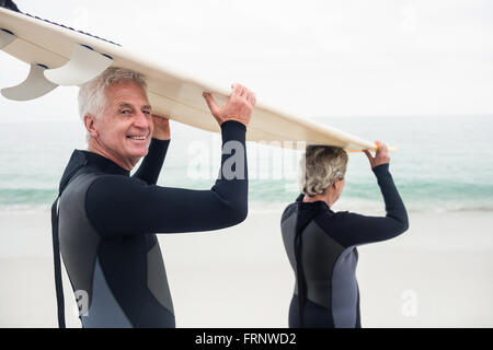 Senior couple in wetsuit surf transport over head Banque D'Images