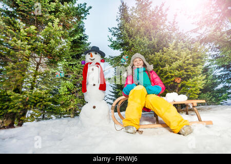 Fille assise sur un traîneau avec Bonhomme à la forêt Banque D'Images