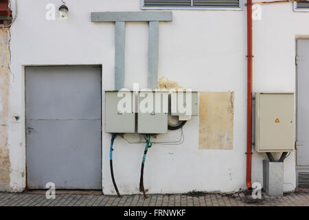 Chaos de fils électriques, des boîtes, des commutateurs et des transformateurs sur un mur d'un hangar en milieu rural Banque D'Images