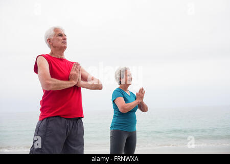 Senior couple in lotus position sur la plage Banque D'Images