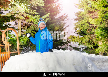 Petit garçon throw snowball se cacher derrière un mur de neige Banque D'Images