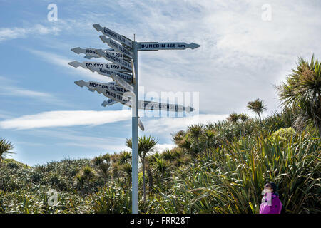 Westport, New Zealand. 25 octobre, 2015. Westport, New Zealand - 25 octobre 2015 - Une femme regarde les panneaux indiquant les distances vers les villes tout autour du monde à Cape Foulwind le 25 octobre 2015 près de Westport, New Zealand. © dpa/Alamy Live News Banque D'Images