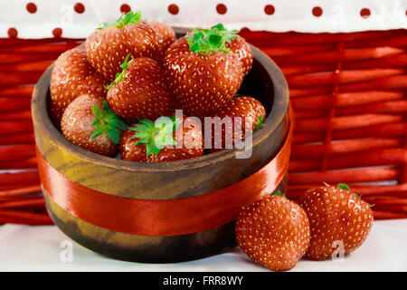 Fraises fraîches dans bol en bois avec fond panier rouge. Banque D'Images