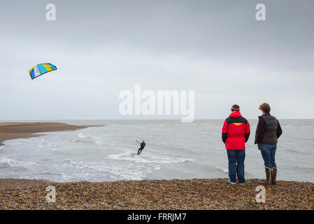 Les gens regardent le kite surf, vue arrière d'un couple se tenant sur Hollesley Beach sur la côte du Suffolk regardant un kite surfeur écumer le rivage, Angleterre Banque D'Images