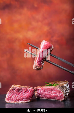 Les steaks. Grill Steak de boeuf. Tranches de faux filet de boeuf steak sur fond de béton sur fourchette à viande. Banque D'Images