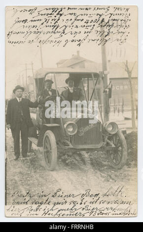 Un groupe d'hommes debout à côté d'une automobile Buick modèle 10 devant l'épicerie animée Bee. La photographie capture un moment de la vie quotidienne dans les rues d’une ville américaine. Banque D'Images