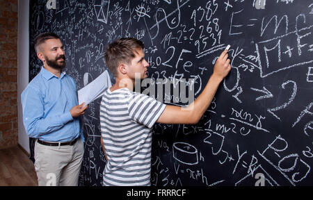 L'enseignant et l'élève écrit le grand tableau noir avec mathematical Banque D'Images