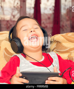 Petite fille sur le canapé avec les écouteurs et la musique d'du smartphone Banque D'Images