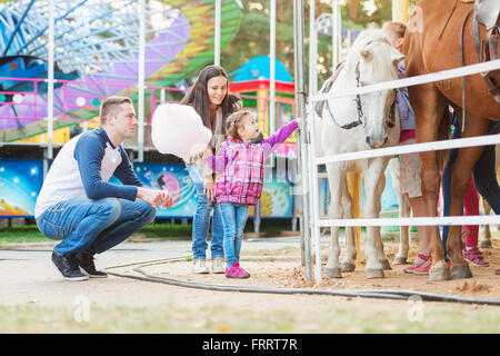 Famille avec fille poney caressant dans amusement park Banque D'Images