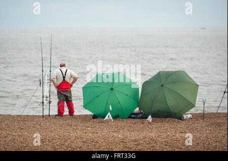 L'homme seul pêche plage, un pêcheur attend patiemment sur la plage de galets près de Hollesley, Suffolk, Angleterre. Banque D'Images