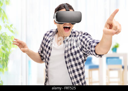 Jeune homme aux prises avec la réalité virtuelle par l'intermédiaire d'un casque VR et atteindre quelque chose avec sa main Banque D'Images
