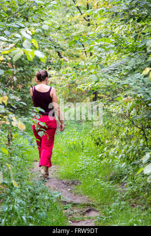 Femme marche le long d'un sentier dans une forêt dense Banque D'Images