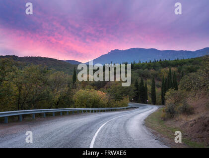 Route sinueuse de montagne en passant par la forêt aux couleurs Ciel et nuages roses au coucher du soleil en été Banque D'Images