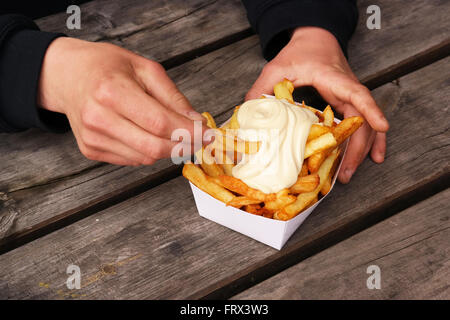 Les mains avec un plateau de frites belges et de la mayonnaise sur le dessus. Banque D'Images