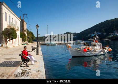 Femme assise sur un banc dans l'idyllique village de pêcheurs avec bateaux de pêche, Kioni, Ithaca, îles Ioniennes, Grèce Banque D'Images