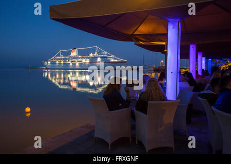 Personnes dans un restaurant le soir avec le bateau de croisière MS Deutschland Peter Deilmann Reederei, à l'embarcadère , Katakolon, Pyrgos, Péloponnèse, Grèce Banque D'Images