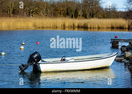 Un petit bateau à moteur hors-bord en plastique amarré dans une baie. Les bouées, l'eau de mer et Reed est dans l'arrière-plan. Un moteur de direction noir wh Banque D'Images