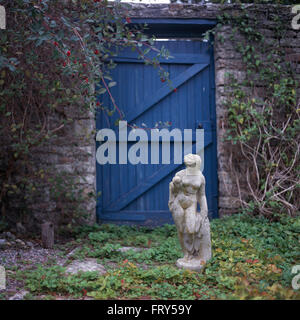 La statue de pierre en face de la porte en bois bleu dans un jardin de campagne fortifiée Banque D'Images